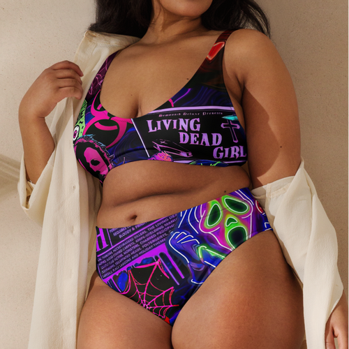 Woman wearing a colorful bikini with a white shirt over her shoulder against a beige wall.